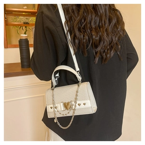 Détail d'un sac bandoulière blanc tressé avec fermoir cœur doré et chaîne élégante décorative