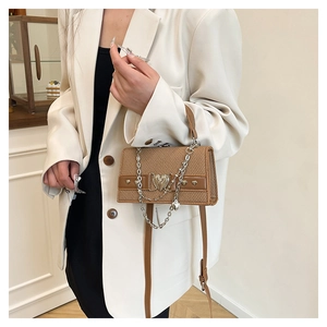 Détail d'un sac bandoulière marron avec boucle coeur argentée porté à l'épaule du mannequin