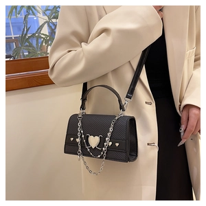 Détail d'un sac à bandoulière noir avec boucle en cœur et chaînes argentées décoratives