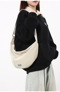 Détail du sac croissant en nylon crème avec bandoulière et logo sur le mannequin
