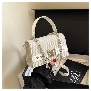 Détail du sac tressé crème avec boucle en cœur et chaîne argentée dans un coffret