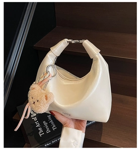 Detailed macro of a creamy white crescent handbag with silver buckle and plush bear charm