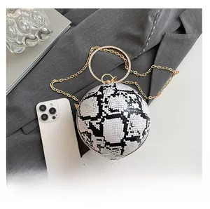 Detail of snake print spherical bag with gold crystal handle beside a smartphone for scale