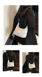 Close-up of minimalist white hobo bag with teddy bear pendant and ribbon detail