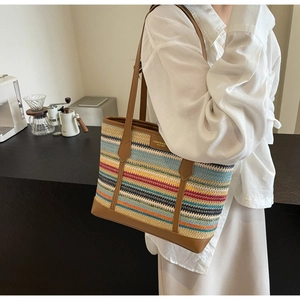 Detail of multi-colored striped woven tote bag with brown leather handles and base