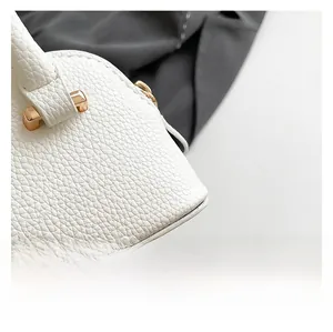 Detailed close-up of white lychee pattern leather handbag and bright gold metal buckle