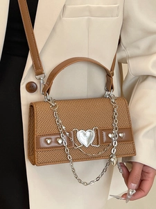 Sac à main tressé marron avec boucle coeur argentée porté sur un blazer beige chic