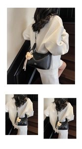 Detail of black leather hobo bag featuring brand logo and plush bear charm pendant