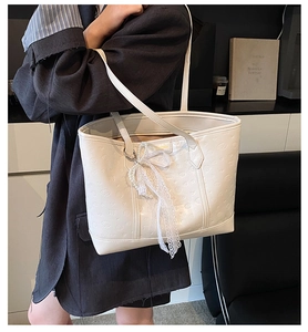 Detail of cream tote bag with embossed texture and lace pearl ribbon accessory