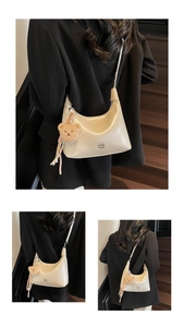 Close-up of beige hobo bag with teddy bear charm and ribbon on dark wood background