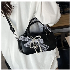 Détail du sac bowling noir avec nœud en dentelle, pendentif perle et foulard en soie