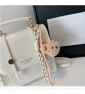 Close-up of cream leather backpack featuring golden logo and cute plush bear charm accessory