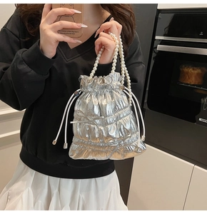 Close-up of a silver metallic bucket bag featuring pearl handles and delicate bow accents