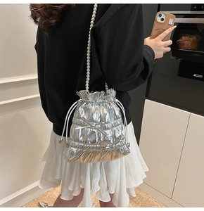 Detail view of silver drawstring bucket bag with pearl strap and bow on woman