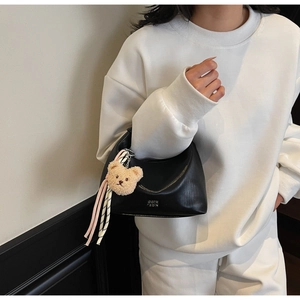 Detail of black crescent bag with bear charm on a model wearing white sweatshirt