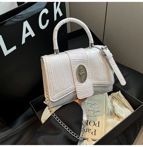 Detail of white crocodile pattern handbag featuring a silver oval twist lock and handle