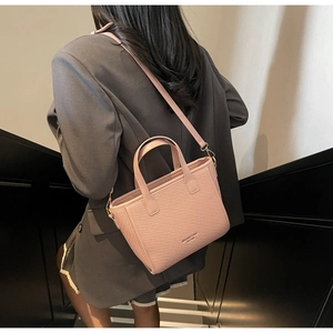 Close-up of pink woven texture crossbody bag with gold hardware and brand logo