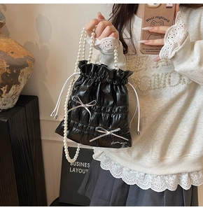 Detail of glossy black pleated bucket bag with silver bows and pearl strap