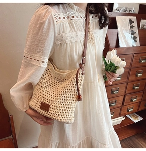 Detail of hand-crochet tote bag with brown leather strap and logo patch on white lace dress