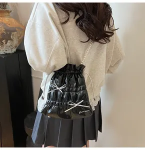 Detail of black glossy drawstring bucket bag with silver bows and pearl bead strap