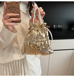 Detail of golden shiny leather bucket bag with pearl handle and bow accents