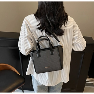 Close-up of black woven leather tote bag with elegant gold branding and smooth leather handles