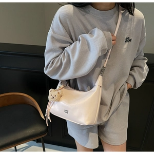Detail of light pink leather crescent bag featuring a brown plush bear charm and metallic logo
