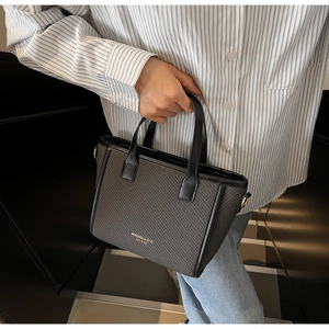 Close-up of woven texture handbag with premium leather handle and brand lettering