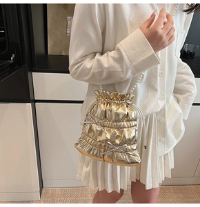 Detail of golden pleated bucket bag with pearl strap and silver bow on white shirt