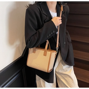 Detail of beige woven bucket bag with brown leather trim worn by a model in a minimal setting