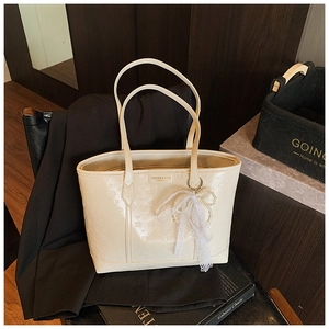 Close-up of cream embossed tote bag featuring lace bow and elegant pearl charm detail