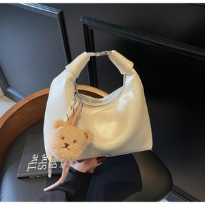 Detail of a creamy white half-moon hobo bag with silver buckle and brown plush bear charm
