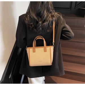Woman in black blazer wearing a khaki woven bucket bag with brown leather trim on stairs