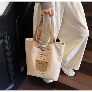 Detail of beige canvas tote bag with embroidered letters and brown ribbon handles