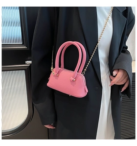 Detailed view of a pink pebbled leather shell bag with golden chain strap on a model