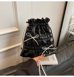 Detail of black glossy drawstring bag with silver bows and elegant pearl chain strap