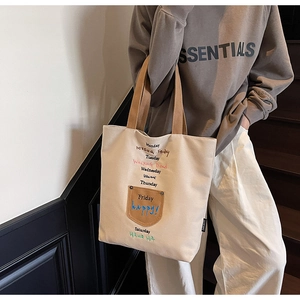 Detail of canvas tote bag with brown pocket, embroidered letters and double handles