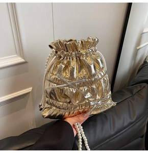 Detail of gold metallic drawstring bucket bag with silver bows and pearl bead strap