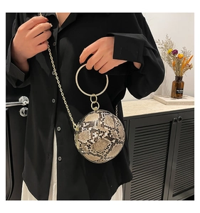 Detail of spherical evening bag with snakeskin pattern and golden ring handle
