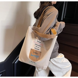 Close-up of beige canvas tote bag with colorful letter embroidery and brown leather pocket