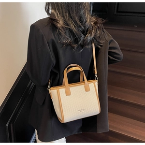 Beige woven bucket bag with brown leather trim carried by a model on wooden stairs