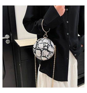 Detail of spherical snakeskin clutch with gold ring handle and chain strap on a model