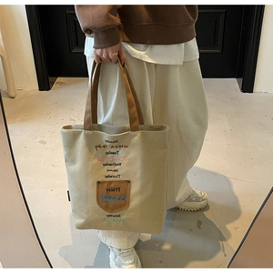 Close-up of canvas tote bag with colorful weekday embroidery and brown leather pocket