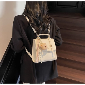 Detail of off-white crocodile embossed backpack with plush bear and decorative scarf