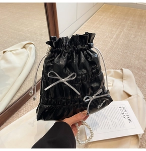 Detail view of black glossy gathered handbag with pearl handle and ribbon bows