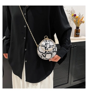 Detailed view of spherical snakeskin bag with golden ring handle and chain strap on model