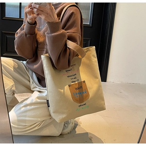 Mirror selfie showing large beige canvas tote bag with embroidered days and leather pocket