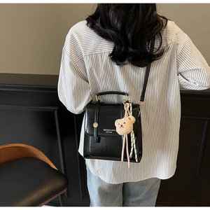 Detail of a black structured backpack with a plush bear charm and brand logo