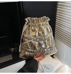 Close-up of metallic gold drawstring bucket bag with pleats and pearl bead strap