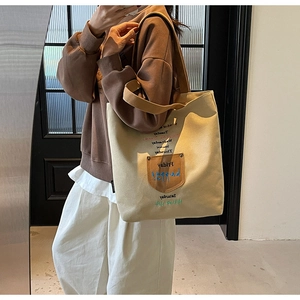 Detail of embroidered canvas tote bag with brown leather pocket and weekday text prints